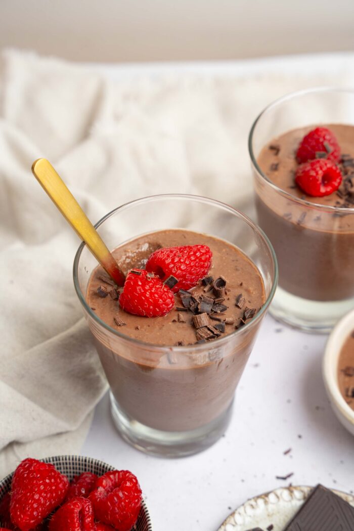 A cup of blended chocolate chia pudding with a spoon sticking out, and another serving visible further in the background.